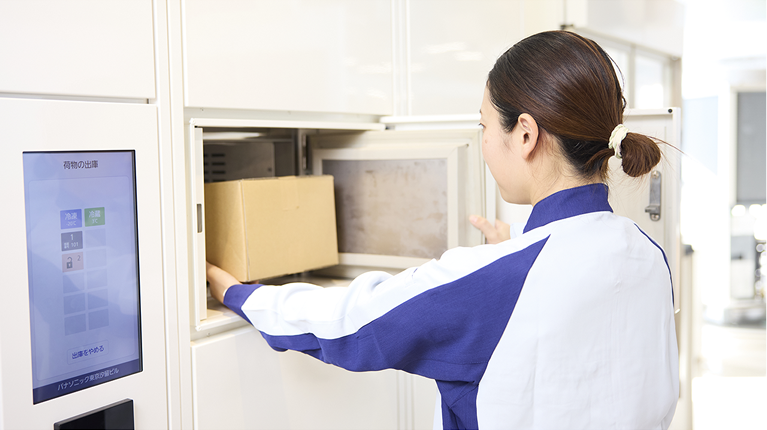 A woman opens the door of a locker and takes out a cardboard box inside.