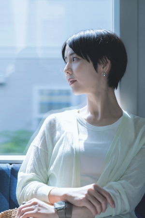 窓から差し込む光を受けて窓の外へ視線をやり、思いにふけている女性