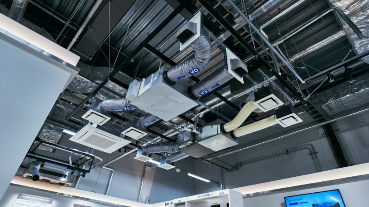 業務用空調・換気システムの天井設置イメージ。天井の骨組みに沿って配置された複数の室内機、換気ユニット、およびそれらをつなぐ銀色のダクト配管の様子。