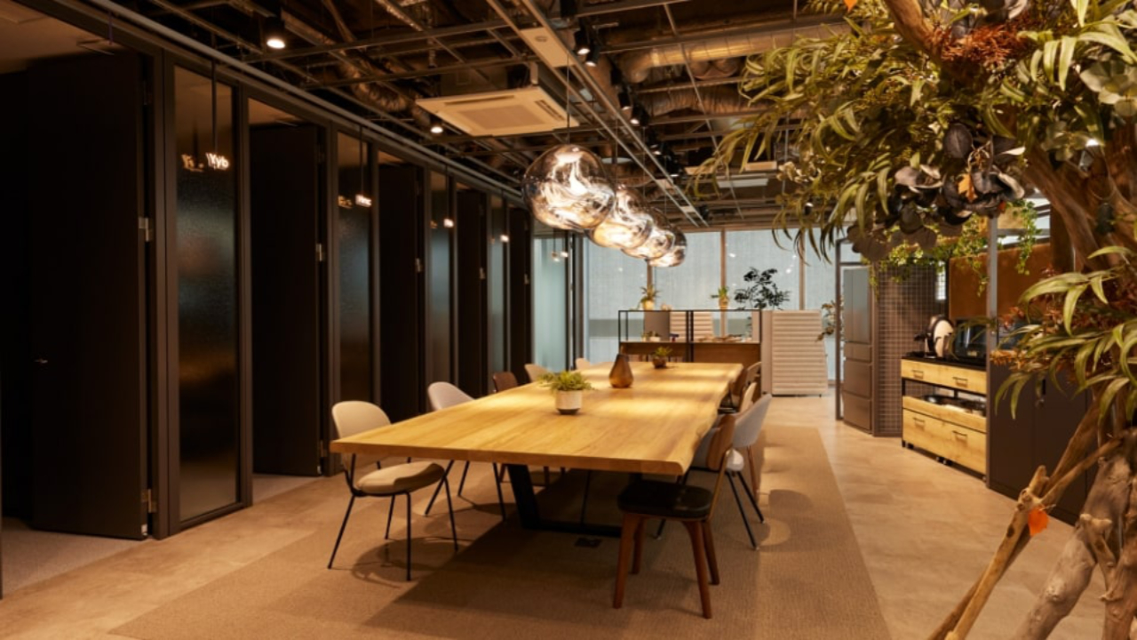 SOLUTIONS GATE OSAKA UMEDA のロゴが入った、木目調のテーブルと緑のある開放的なオフィス空間