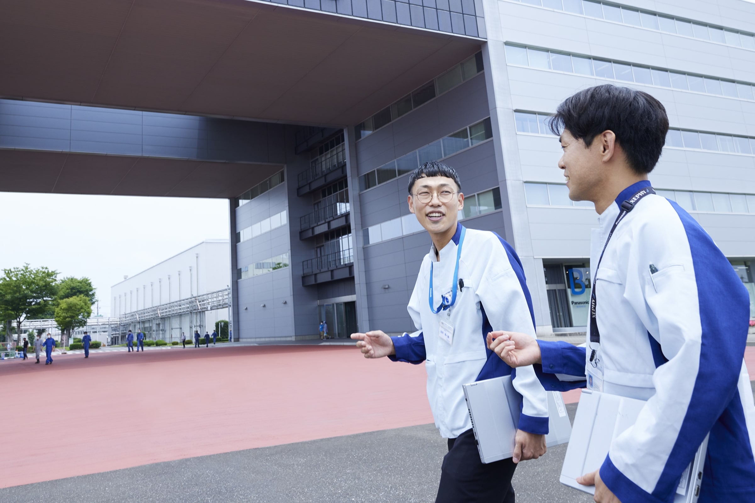 採用トップページキービジュアル画像2。男性社員2人が話しながら歩いている様子。