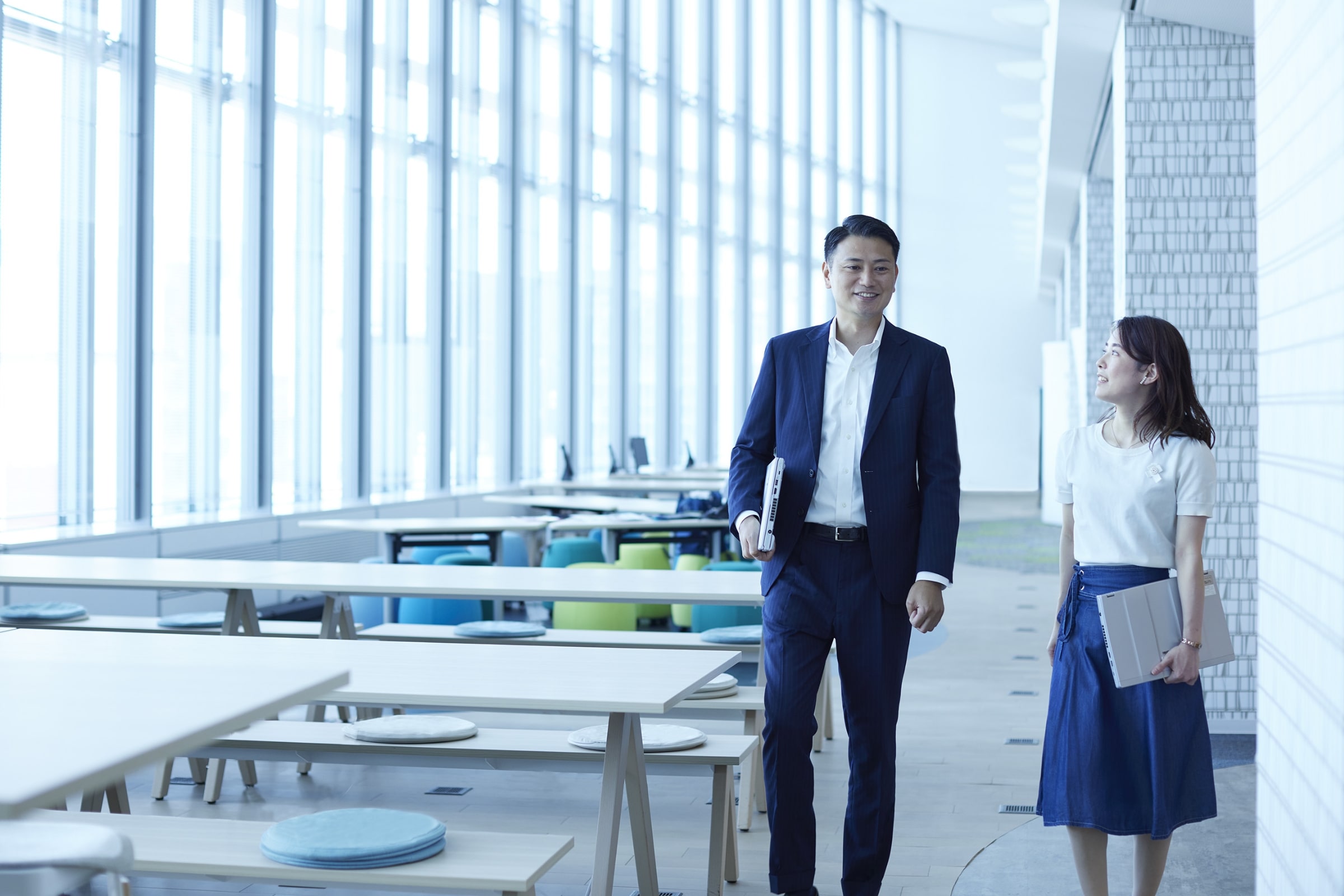 採用トップページキービジュアル画像3。男女2名の社員が社内で話しながら歩いている様子。