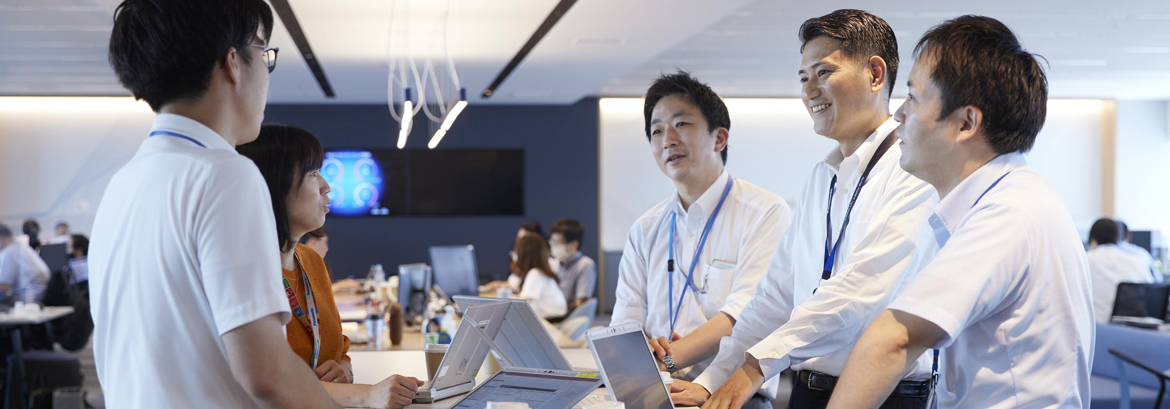 ノートパソコンを開きながら同僚達と談笑する壬生の画像