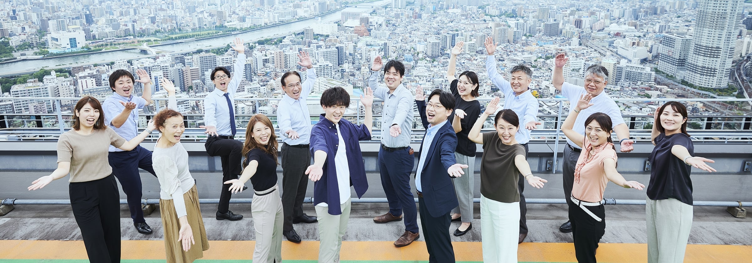 景色のよい屋上で笑顔で手を広げる男女スタッフの集合画像