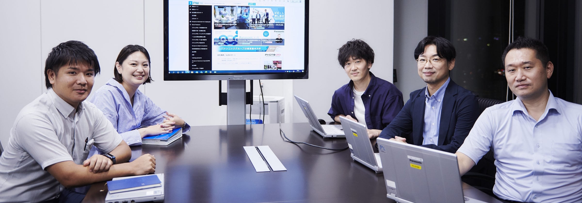 会議室でモニターを中心にテーブルにつく男女スタッフの集合画像