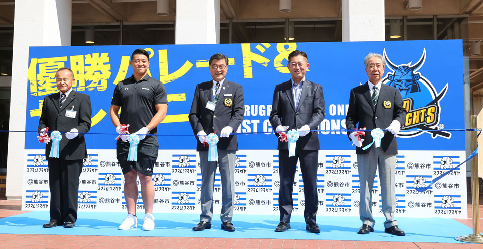画像:スタート地点の熊谷市役所前でテープカット。左から福田勝美市議会議長、坂手選手、小林市長、久保田代表、大久保和政商工会議所会頭